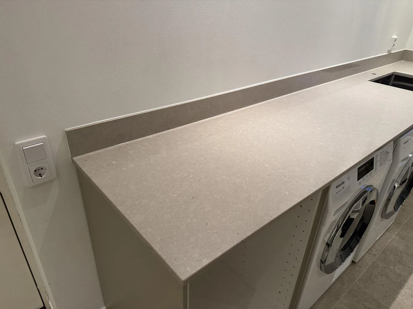 Lång bänkskiva i polerad Silestone Royal Reef med 12 mm stänkkant och öppna stommar över maskiner i Höllviken.