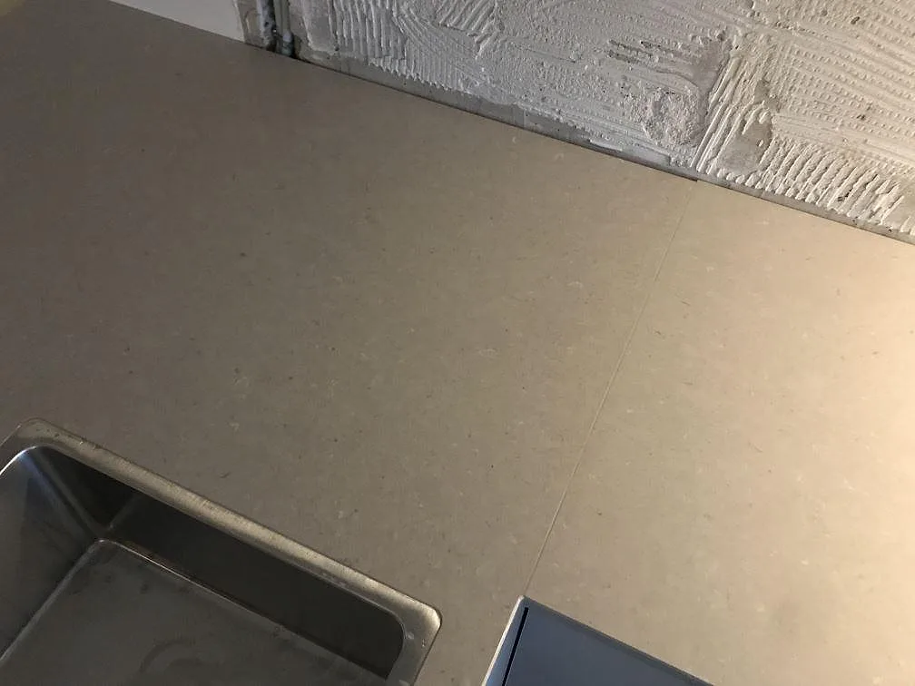 Hörnparti av bänkskiva i Silestone Royal Reef med rostfri diskho mot oputsad vägg under montering i Jönköping.