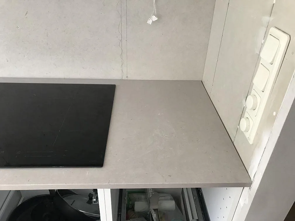 Hörnparti av köksbänk i beige Silestone Royal Reef med induktionshäll och eluttag, monterad mot omålad vägg i Karlskrona.
