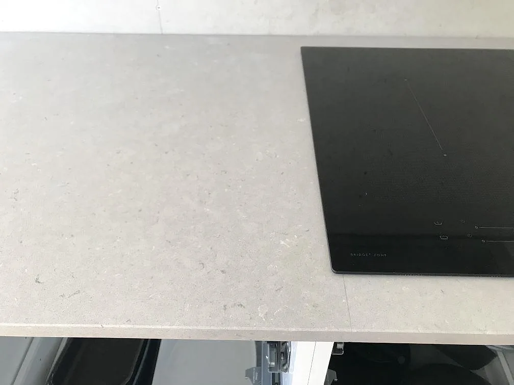 Bänkskiva i Silestone Royal Reef med induktionshäll på plats och öppna stommar under, polerad beige komposit i ett kök i Karlskrona.