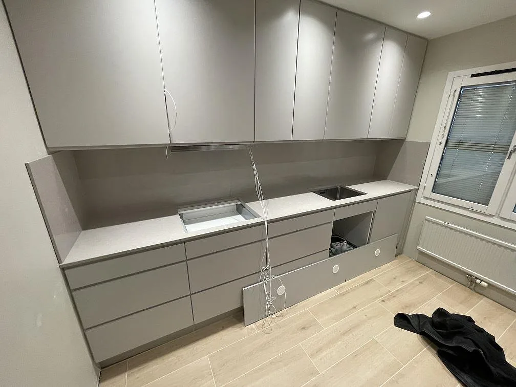 Köksbänkskiva i ljus Silestone Royal Reef, polerad kvartskomposit, med uppvikt stänkskydd i samma sten, urtagning för diskho och plats för häll i ett kök under montering i Kista.