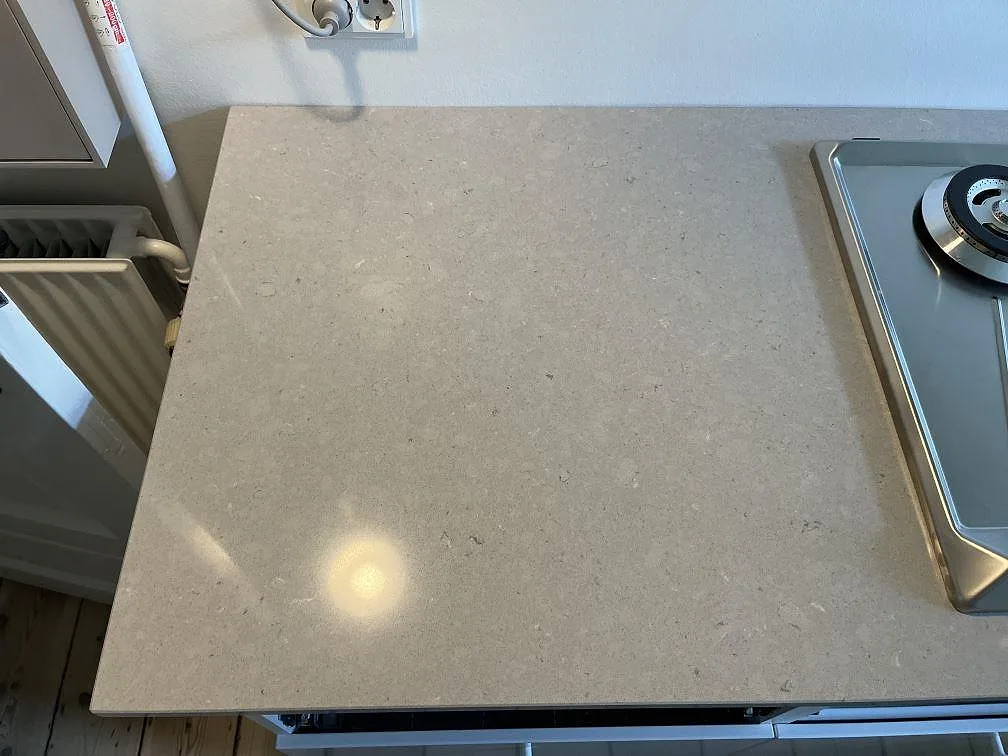 Sandbeige köksbänkskiva i polerad Silestone Royal Reef vid värmeelement och fönster, med gashäll till höger, i ett kök i København N.