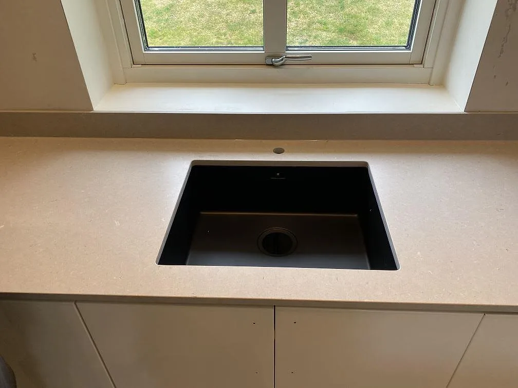 Underlimmad svart kompositdiskho monterad under bänkskiva i matt Silestone Royal Reef i ett kök i Kristianstad.
