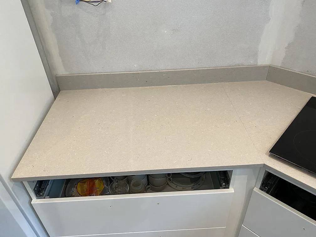 Vinklad bänkskiva i sandbeige Silestone Royal Reef med infälld induktionshäll och uppvikt stänkkant i ett kök i Kristianstad.