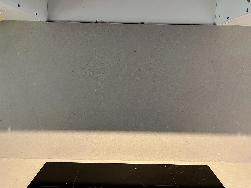 Stänkskydd i ljus beige Silestone Royal Reef komposit ovanför svart häll i kök i Limhamn.