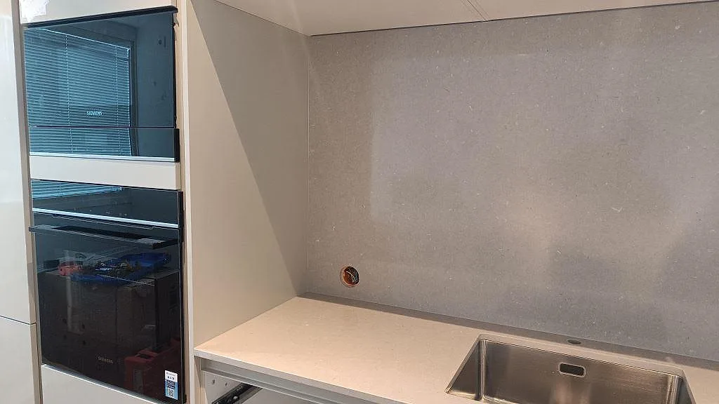 Köksbänkskiva i polerad Silestone Royal Reef bredvid högskåp och grå väggbeklädnad i ett kök i Limhamn.