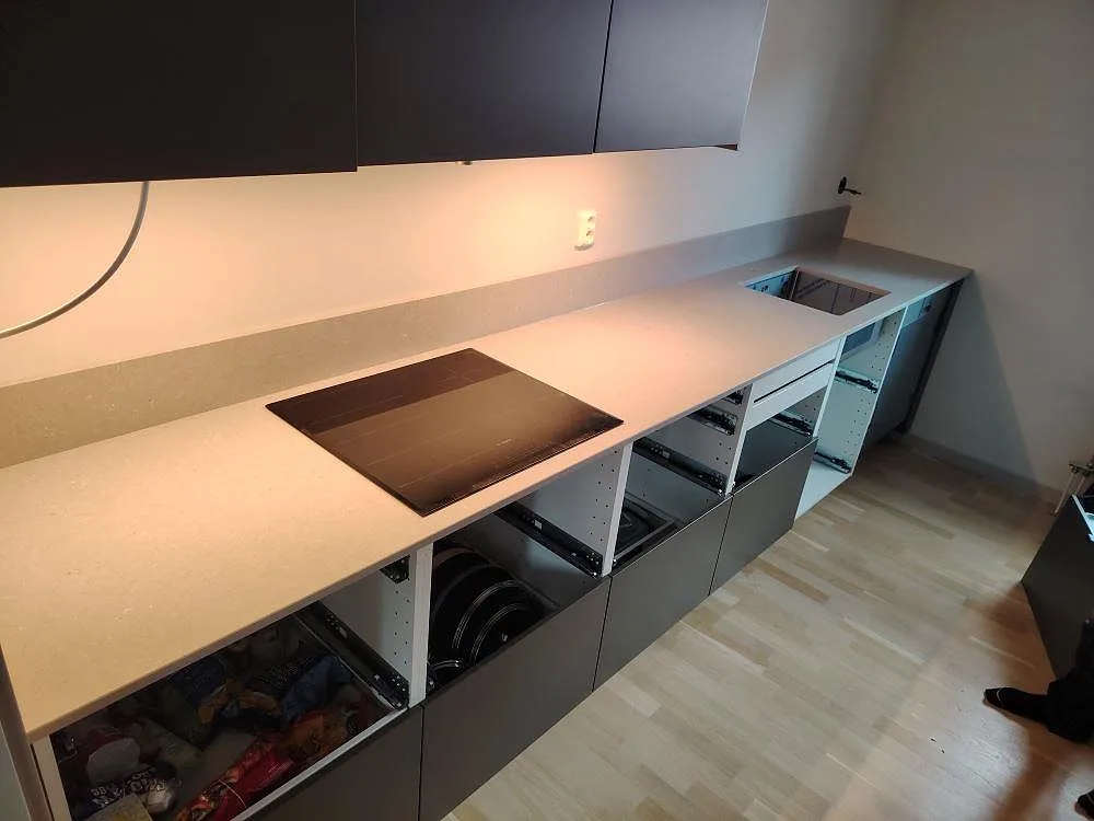 Köksbänkskiva i ljus gråbeige Silestone Royal Reef komposit, matt Mocka, med induktionshäll och diskhoöppning i ett kök under montering i Linköping.