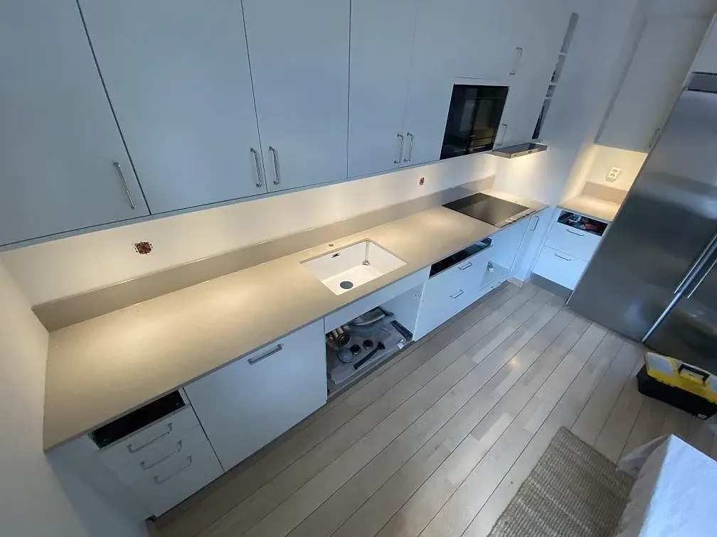 Köksbänkskiva i beige Silestone Royal Reef, polerad, längs en sammanhängande bänkrad med vit underlimmad diskho och infälld induktionshäll i ett kök i Lund.