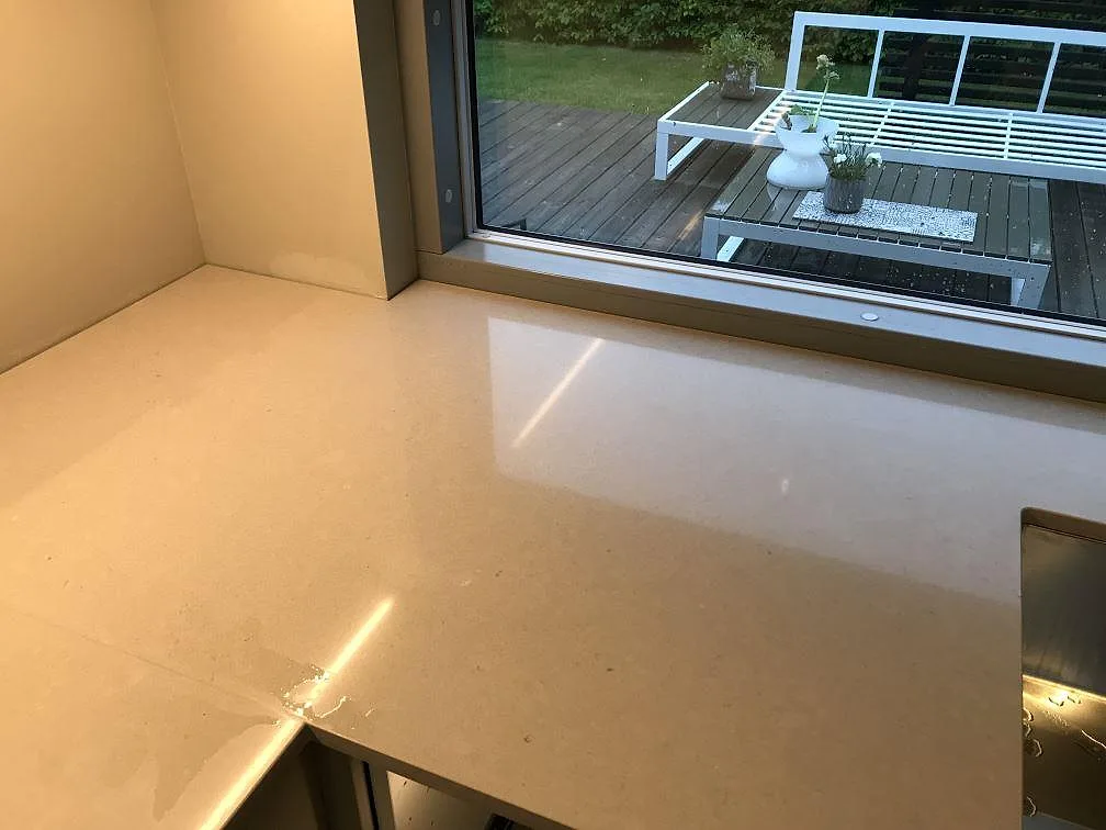 Köksbänkskiva i krämvit Silestone Royal Reef, polerad, i ett U-format kök i Malmö med greppfria taupe luckor, underlimmad rostfri diskho och urtagning för induktionshäll.