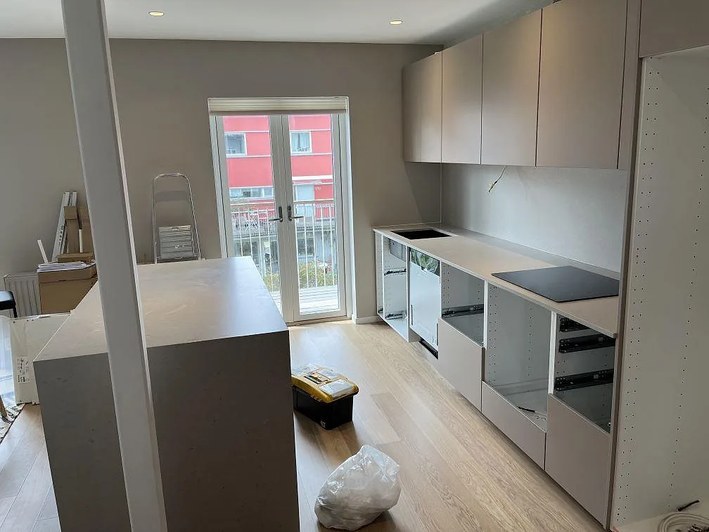 Köksbänkskiva och köksö i greige Silestone Royal Reef kvartskomposit i ett kök under montering i Malmö med balkongdörr och ljust trägolv.