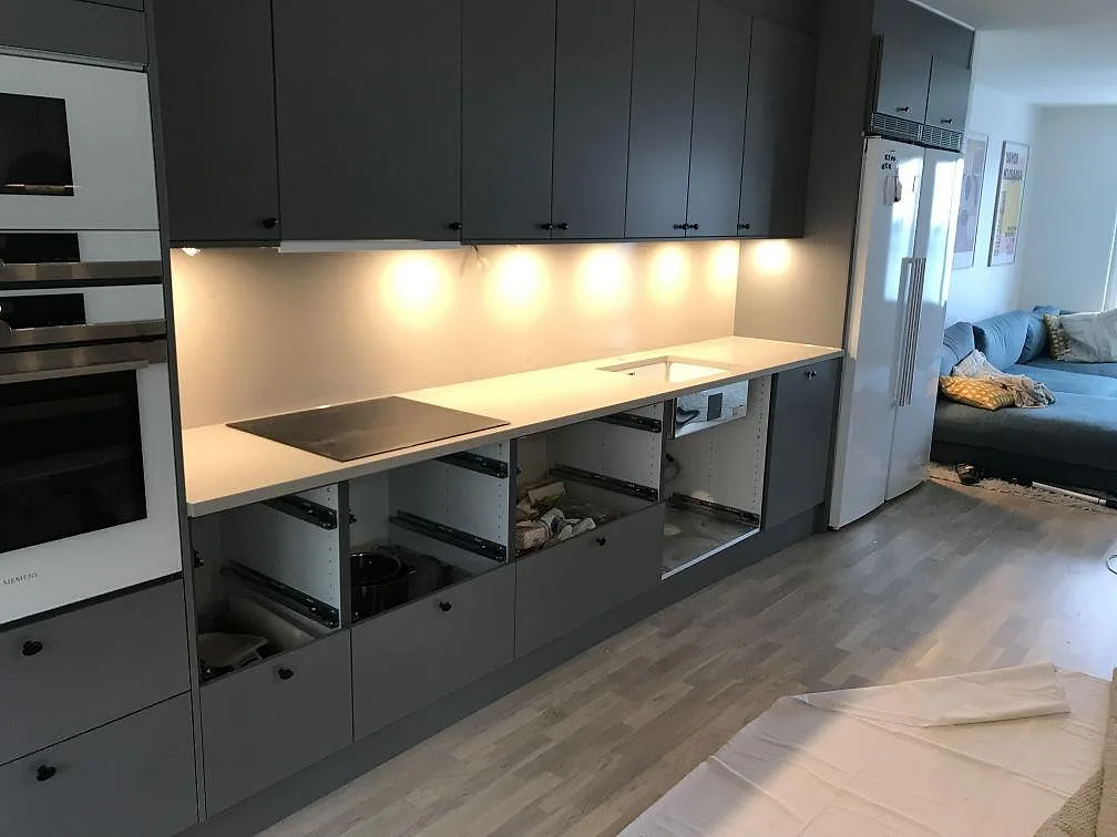 Köksbänkskiva i beige Silestone Royal Reef, polerad, med infälld induktionshäll och heltäckande stänkvägg mot mörkgrå köksluckor i ett kök i Malmö.