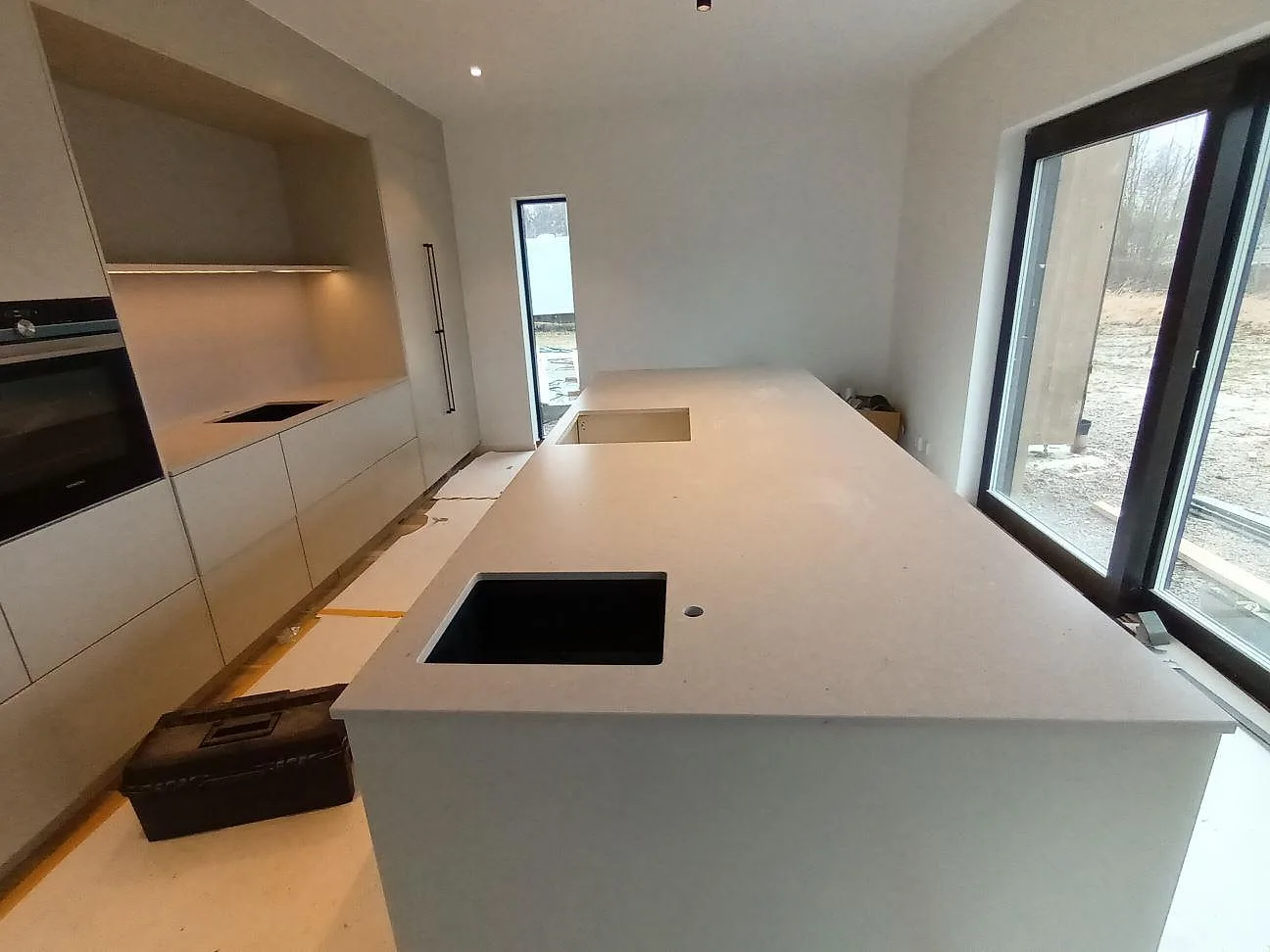 Köksbänkskiva och stor köksö i beige Silestone Royal Reef, matt Mocka, med underlimmad svart kompositdiskho i ett kök i Örebro.