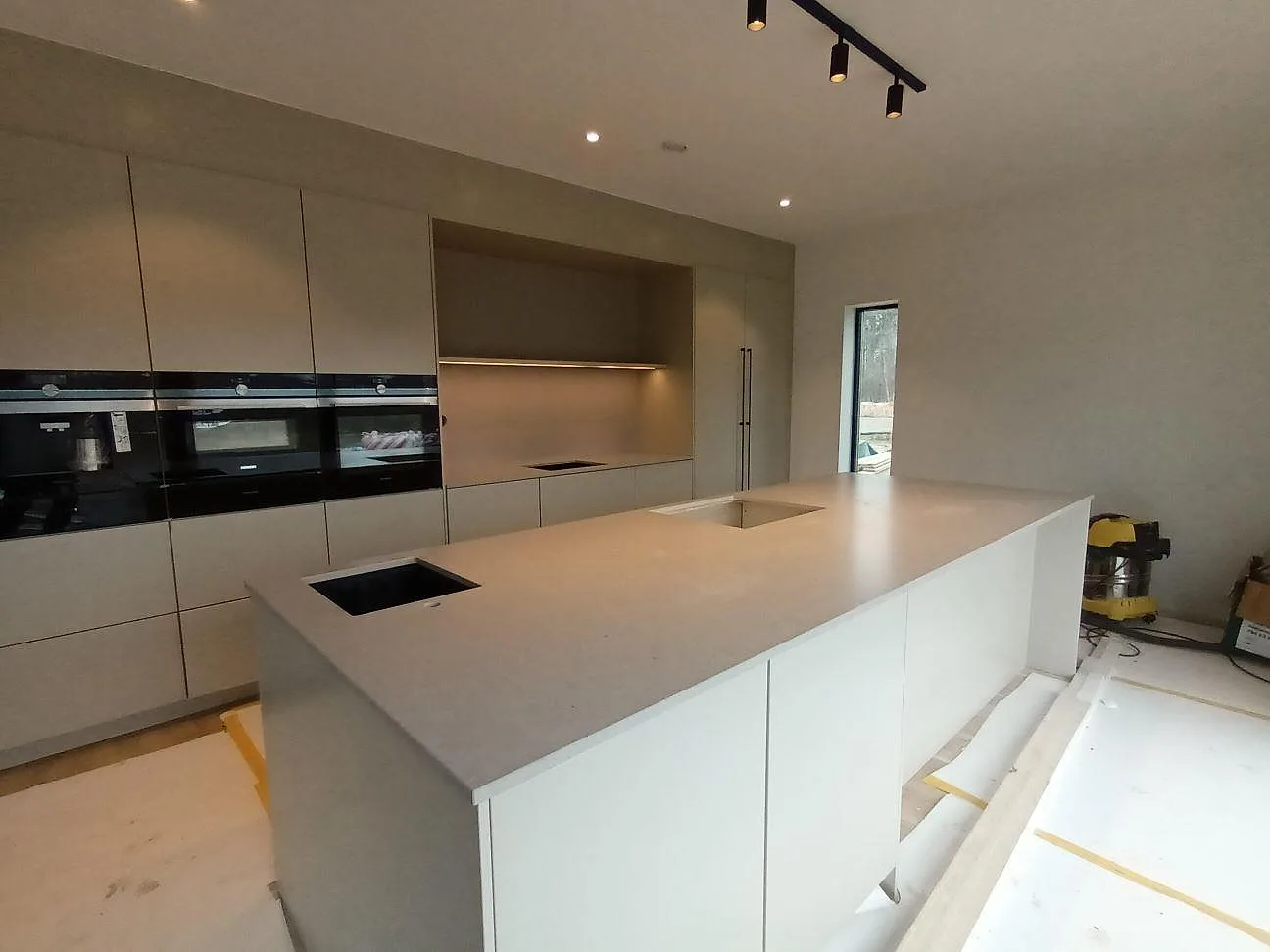 Köksö i beige Silestone Royal Reef med urtag för diskho och induktionshäll, matt yta, framför mörka inbyggnadsugnar i ett kök i Örebro.