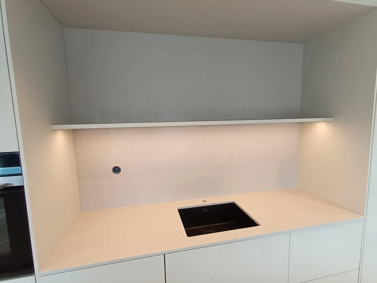 Beige köksbänkskiva i Silestone Royal Reef med uppvikt stänkskydd och underlimmad svart diskho i en köksnisch i Örebro.