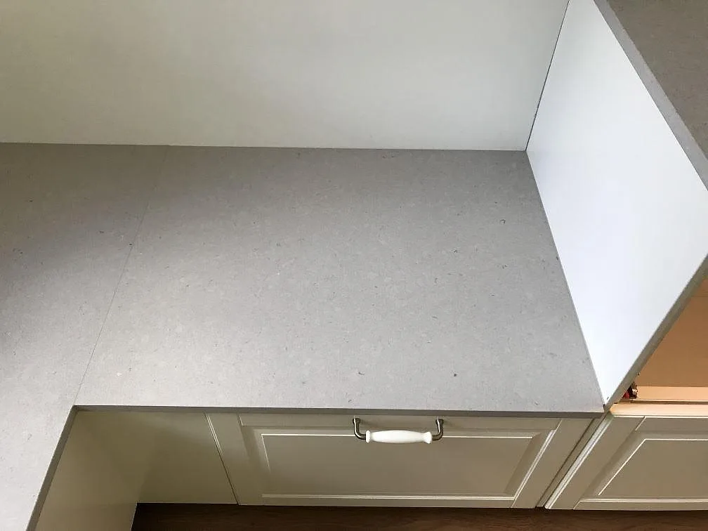 Köksbänkskiva i ljust gråmelerad Silestone Royal Reef, matt Mocka-finish, monterad på krämfärgade köksstommar i ett kök i Olofström.