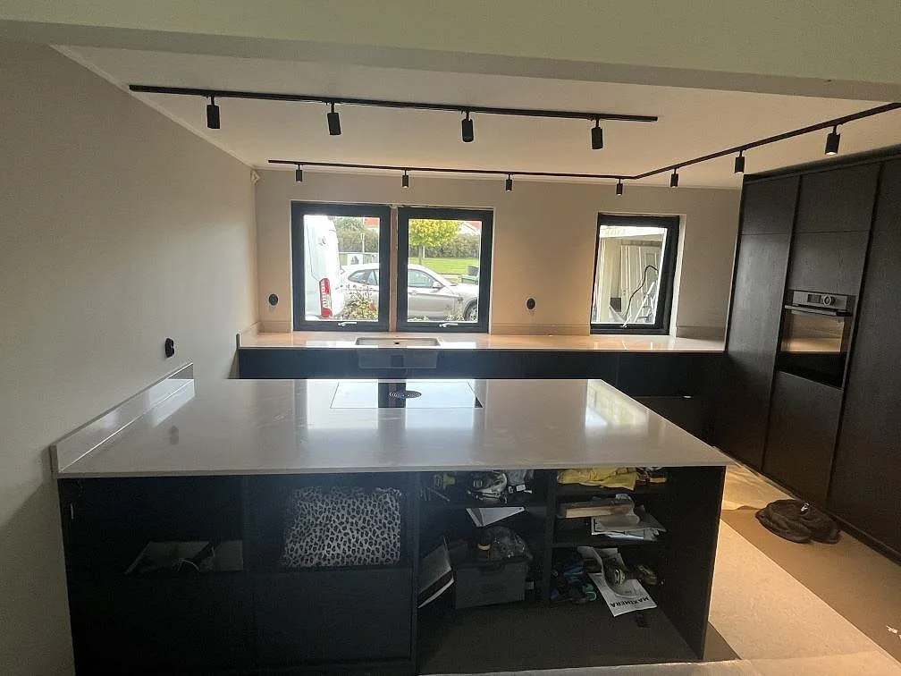 Köksbänkskiva och köksö i Silestone Royal Reef, polerad beige kvartskomposit, i ett ljust kök under montering med insatt induktionshäll och stora fönster i Rydebäck.