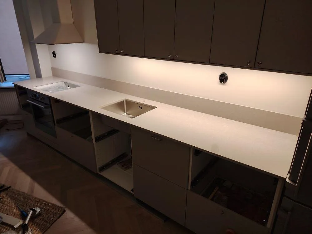 Köksbänkskiva i ljus Silestone Royal Reef komposit, polerad, med matchande stänkskydd och urtag för diskho och häll i ett kök i Stockholm.