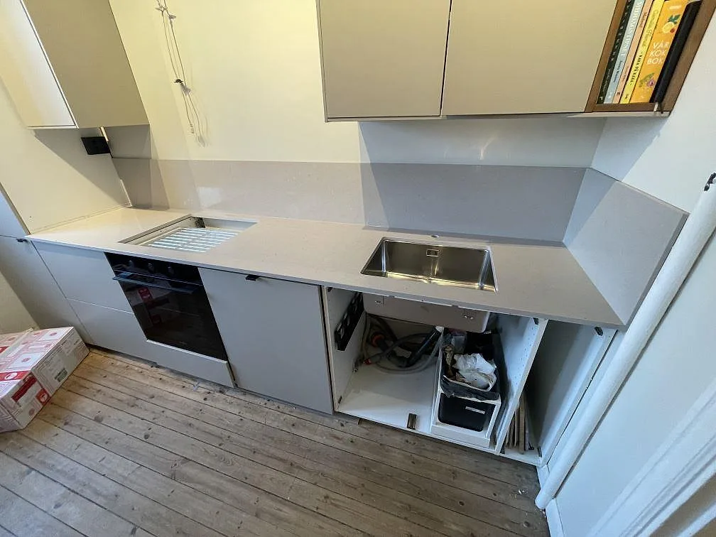Rak köksbänk i ljusgrå Silestone Royal Reef under montering, med frästa avrinningsspår, rostfri diskho och inbyggd ugn i ett kök i Stockholm.