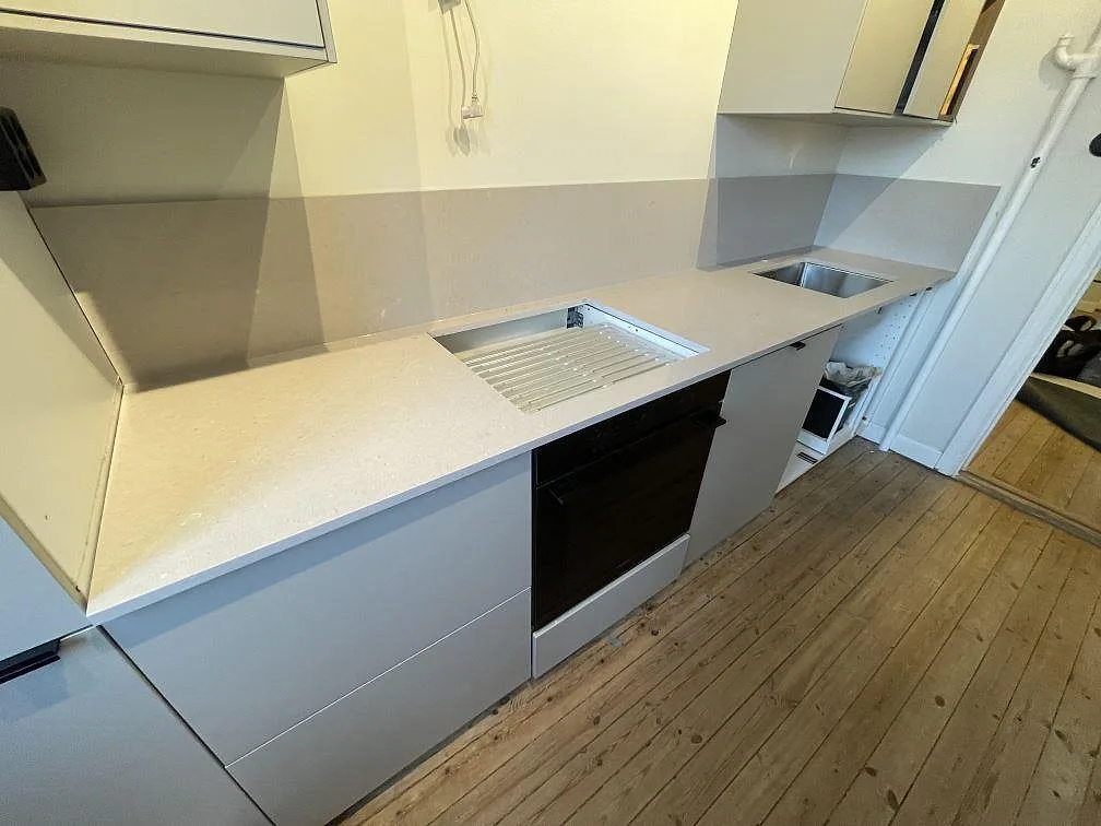 Köksbänkskiva i krämig Silestone Royal Reef, polerad, med räfflad avrinningsyta och underlimmad rostfri diskho längs en rak köksbänk i ett kök i Stockholm.