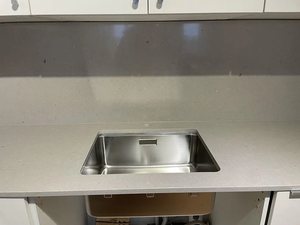 Underlimmad rostfri diskho infälld i polerad Silestone Royal Reef köksbänkskiva, med ett varmare stänkskydd i Silestone Coral Clay bakom, i ett kök i Stockholm.