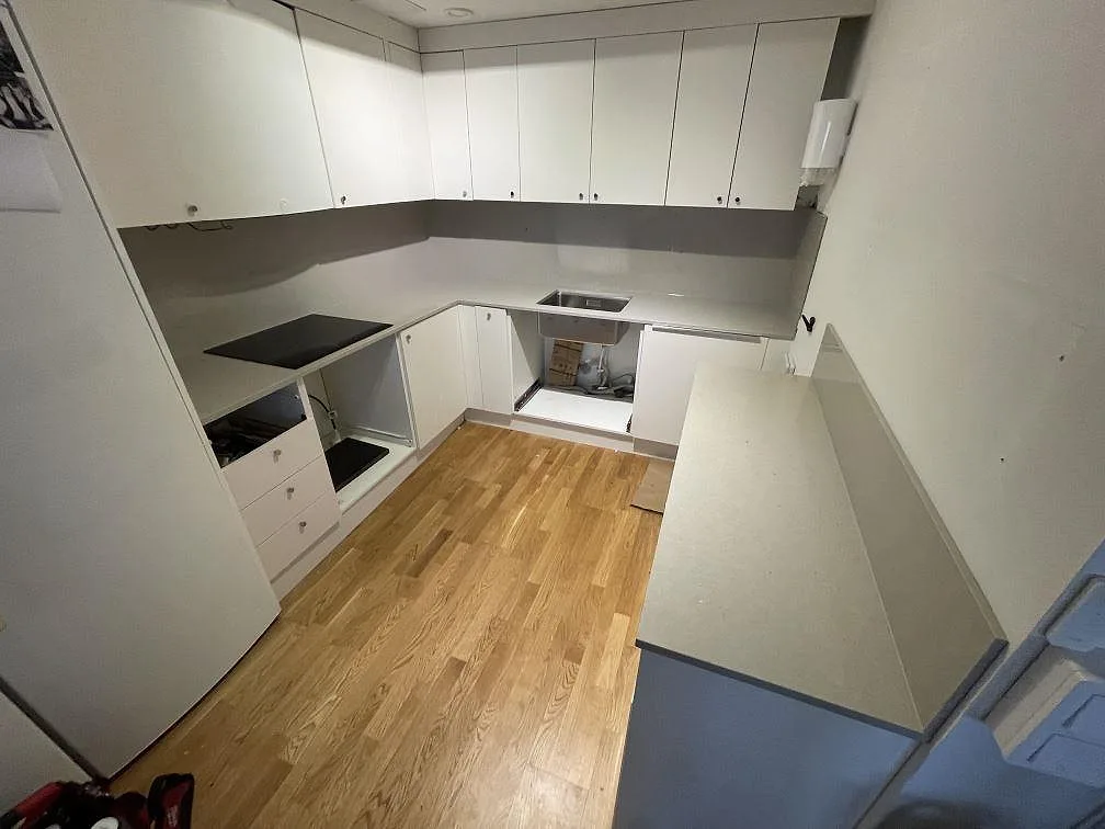 Köksbänkskiva i ljust beige Silestone Royal Reef, polerad kvartskomposit, i ett U-format kök i Stockholm med svart induktionshäll och underlimmad rostfri diskho under montering.