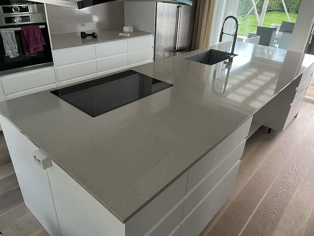 Köksö i polerad Silestone Royal Reef, greige kvartskomposit, med synlig häll och mörk blandare i ett kök i Täby.