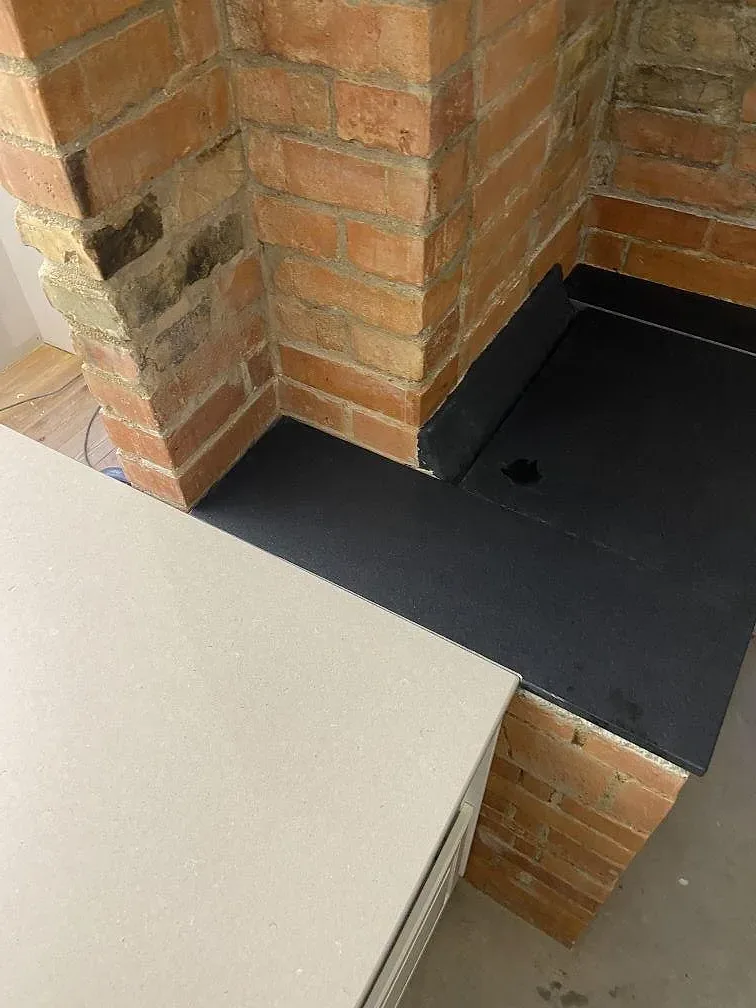 Hörn där bänkskivan i Silestone Royal Reef möter eldstadens granithäll och tegelskorstenen i ett kök i Tjurkö.