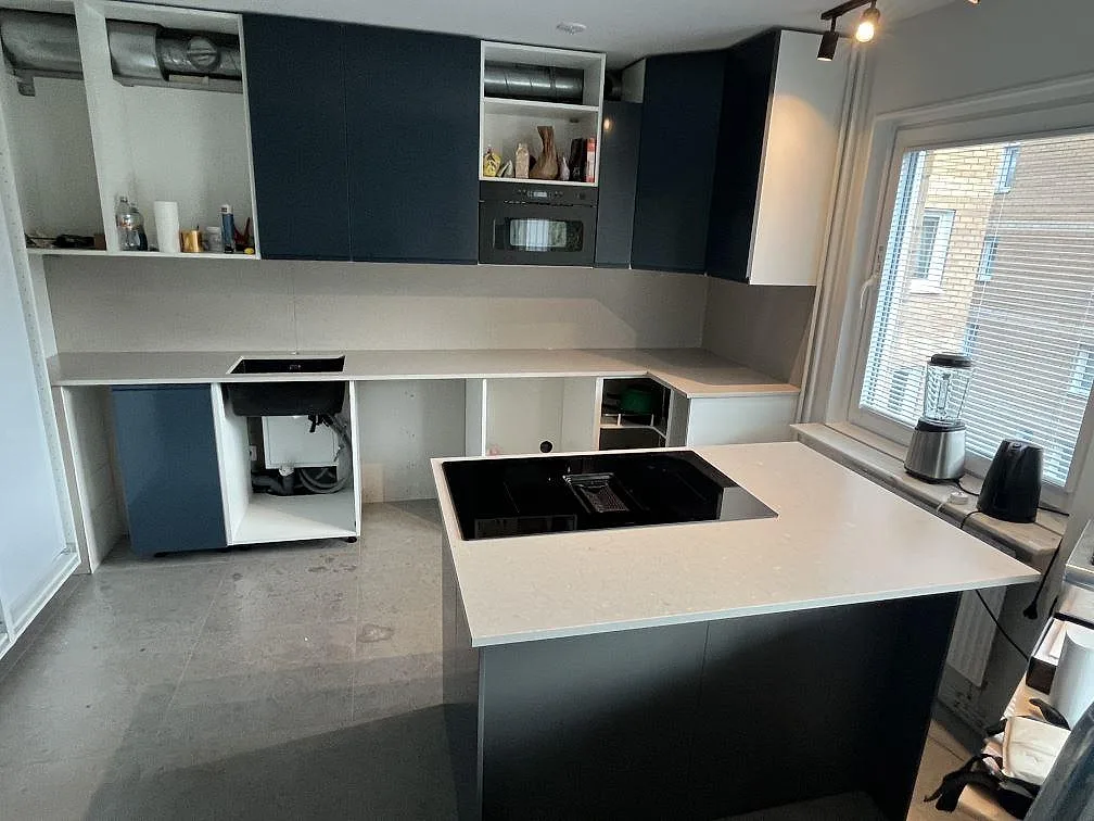 Köksbänkskiva i ljus Silestone Royal Reef, matt Mocka komposit, med köksö, svart induktionshäll och blå köksluckor i Tyresö.