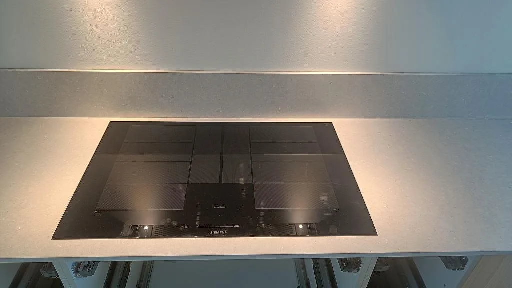 Svart induktionshäll monterad i matt Silestone Royal Reef med matchande låg stänkkant i köket i Uddevalla.