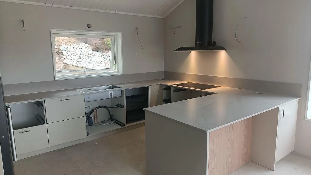 Köksbänkskiva och köksö i matt Silestone Royal Reef med låg stänkkant, svart häll och fläktkåpa i ett kök i Uddevalla.