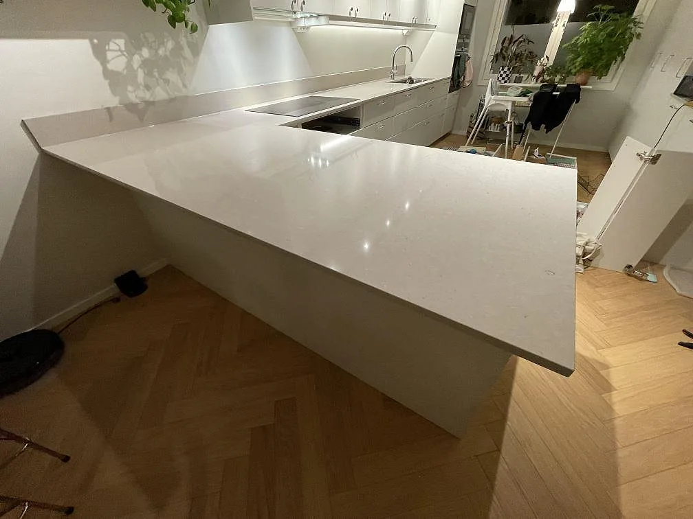Köksbänkskiva i ljus Silestone Royal Reef, polerad kvartskomposit, med synlig rostfri diskho och häll i ett kök i Uppsala.