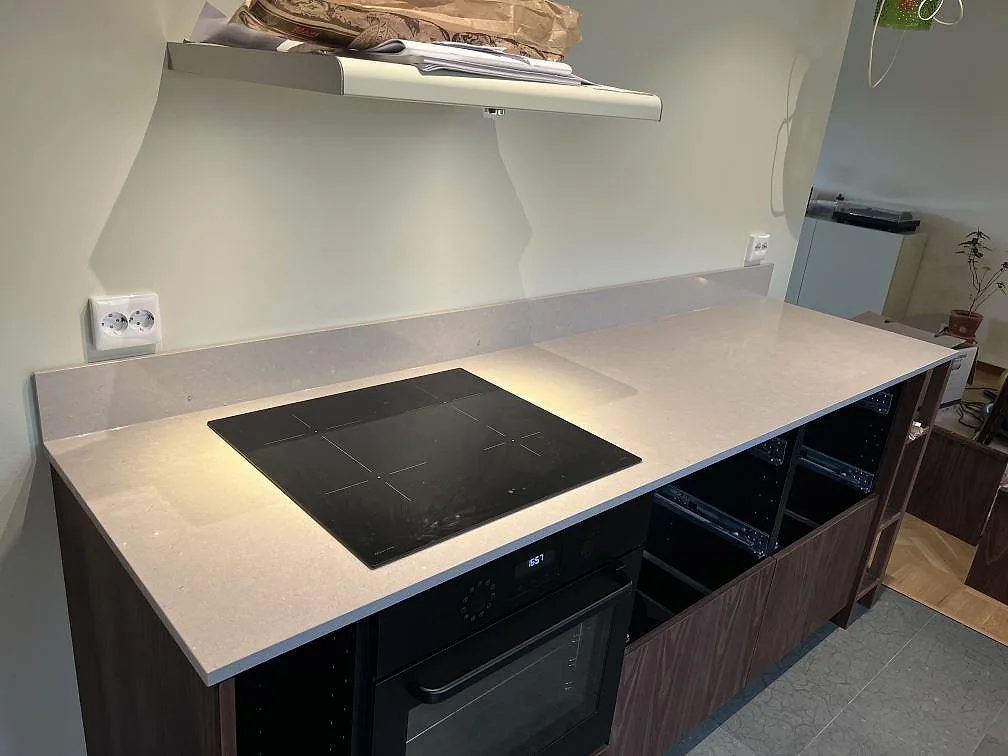 Köksbänkskiva i beige Silestone Royal Reef, polerad, med infälld induktionshäll och uppvikt stänkkant i ett kök under montering i Växjö.