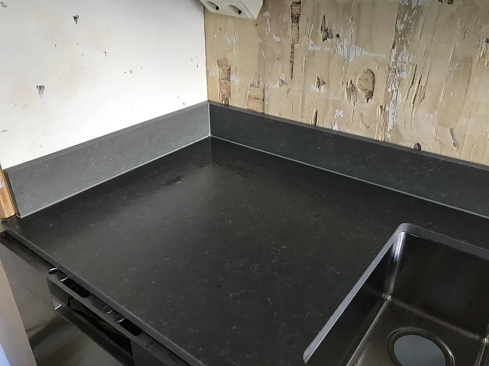 Hörn av köksbänkskiva i grå Silestone Seaport med uppvikt stänkkant och underlimmad rostfri diskho, matt mocka yta, kök i Hisings-Kärra.