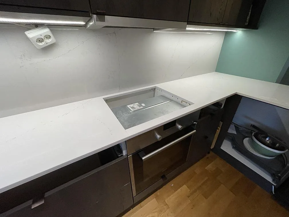 Detalj av hällöppning i polerad Silestone Siberian frost med ljus stänkvägg och mörka köksluckor under montering i Bromma.