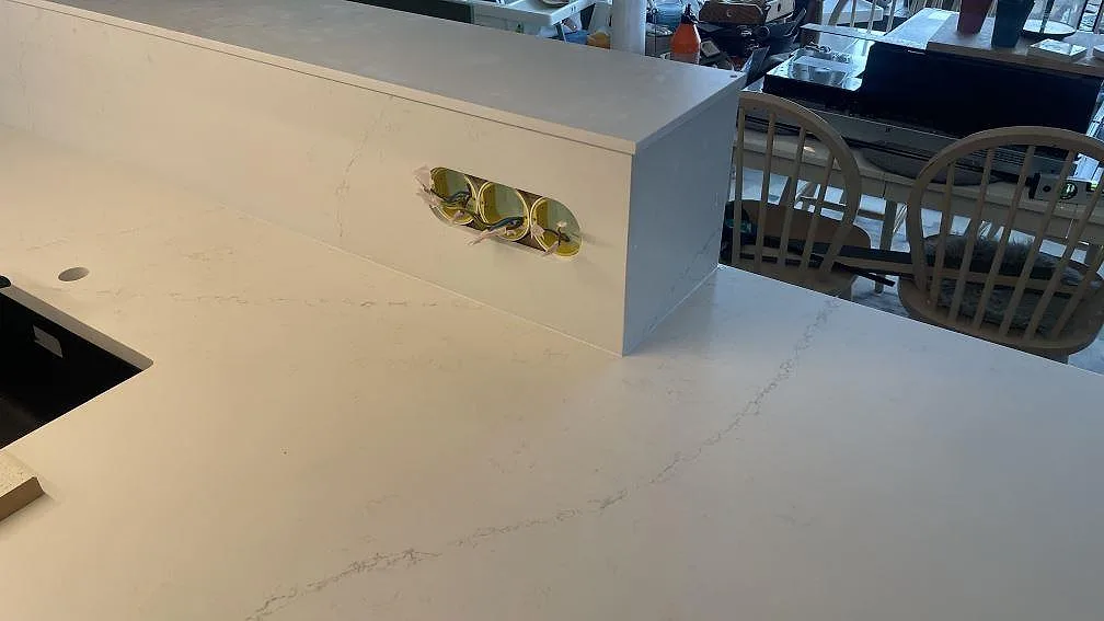 Köksö i matt Silestone Siberian frost med grå ådring, upphöjd stenpanel och eluttag under montering i Jönköping.