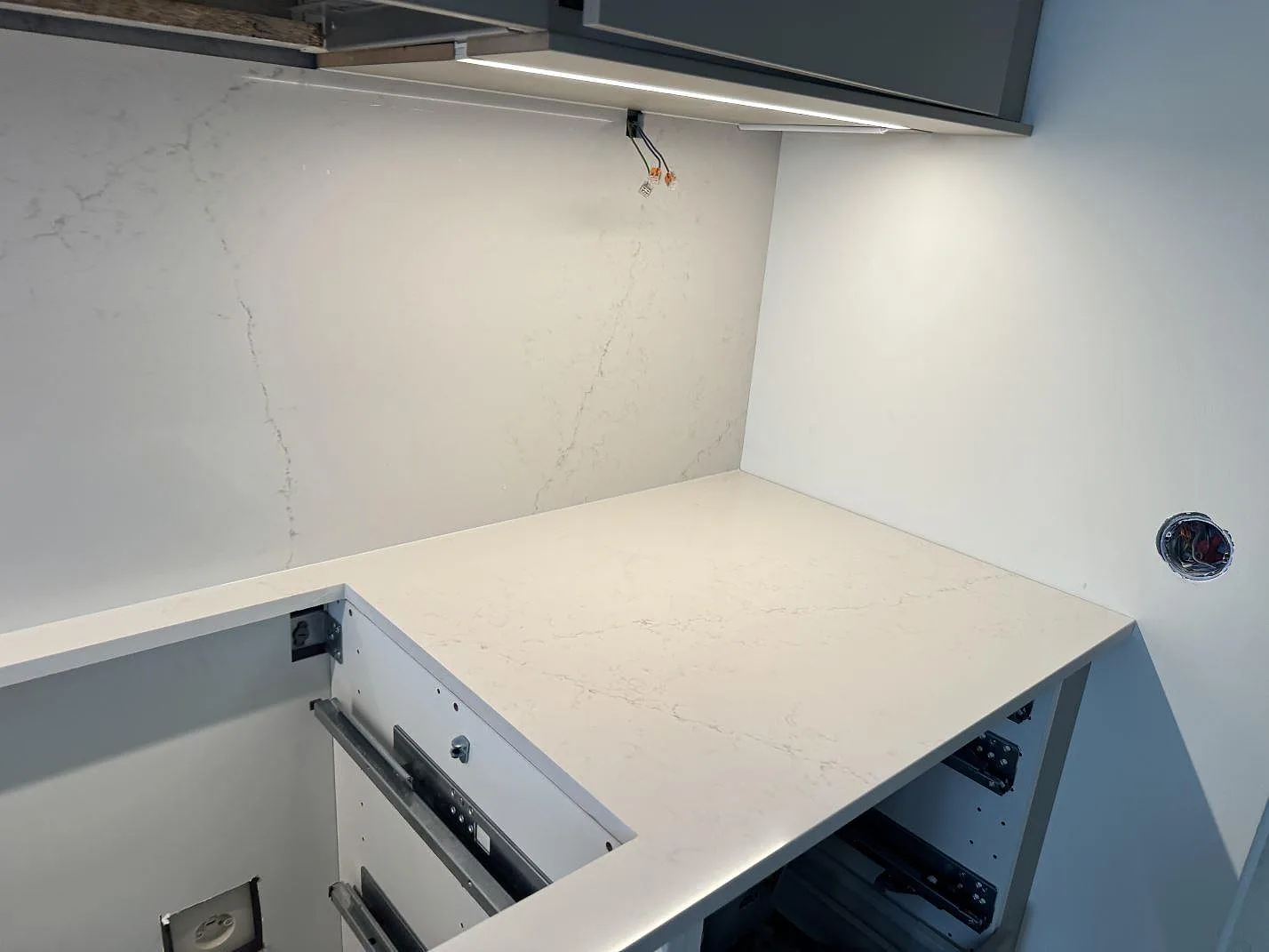 Ljus köksbänkskiva i Silestone Siberian frost, polerad, med väggbeklädnad och urtag under köksfläkten i Limhamn.