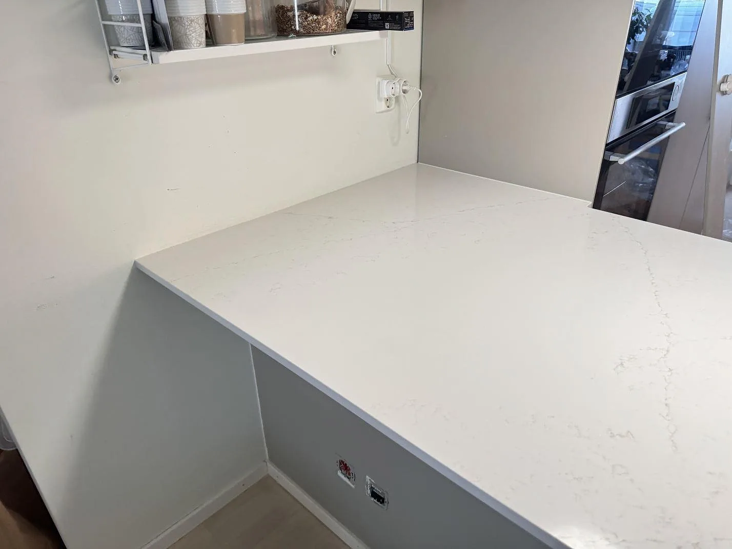 Detalj av polerad Silestone Siberian frost på större köksbänk med ljus ådring och ugn i bakgrunden i Limhamn.