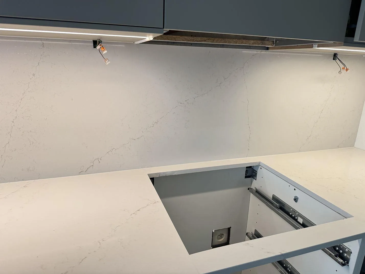 Köksbänkskiva och matchande väggbeklädnad i polerad Silestone Siberian frost under köksskåp i Limhamn.