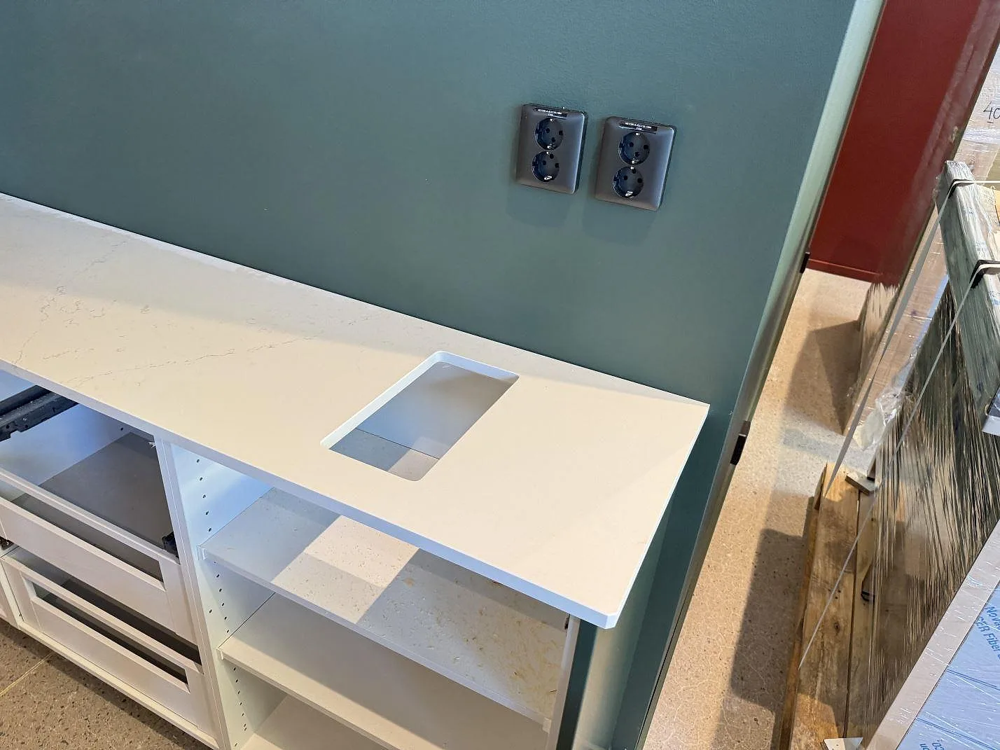 Detalj av rektangulärt urtag i polerad Silestone Siberian frost, ljus kompositskiva monterad mot grön vägg i Malmö.
