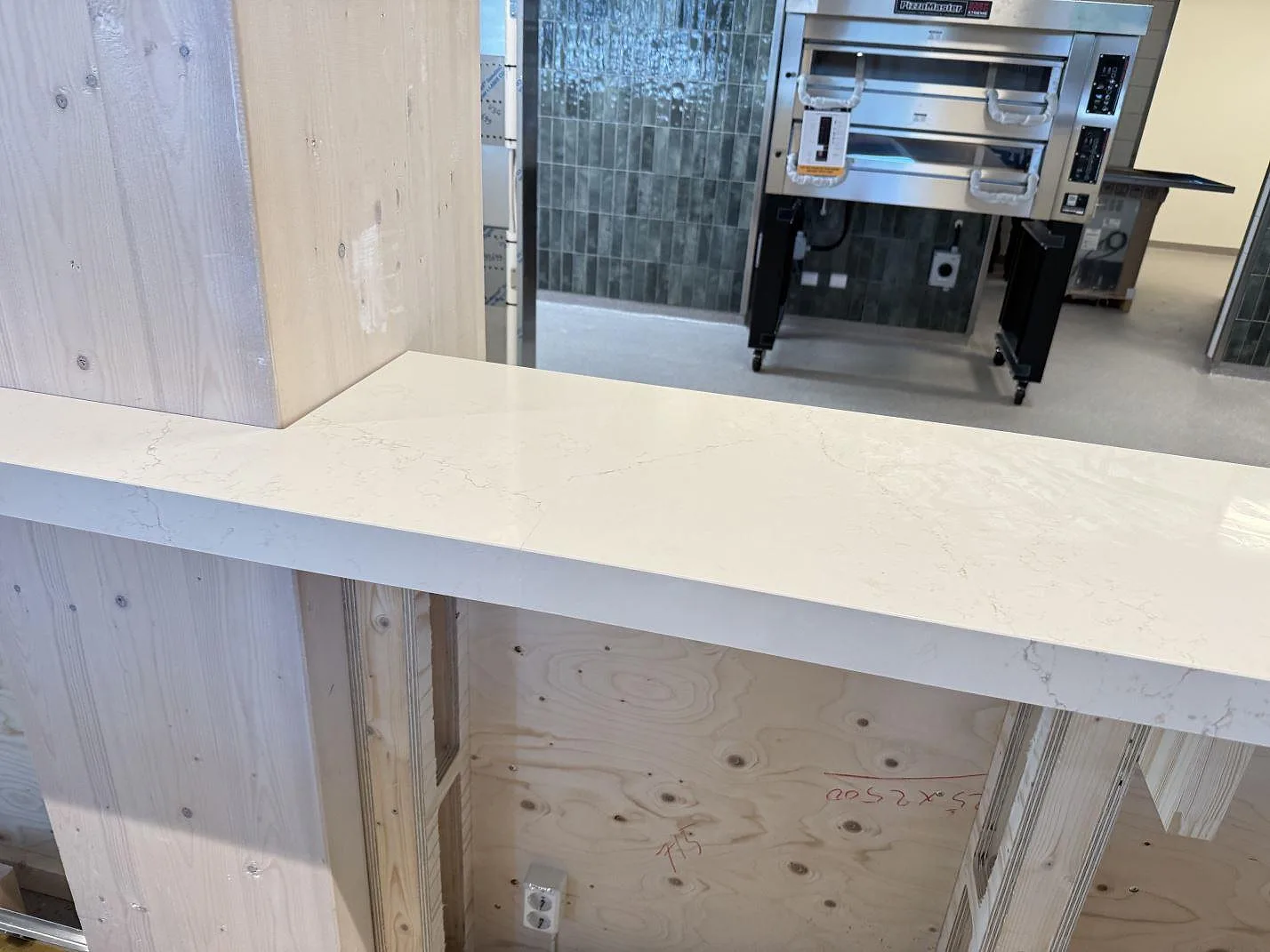 Närbild på polerad Silestone Siberian frost som ljus bänkskiva runt träinredning i ett kök under montering i Malmö.