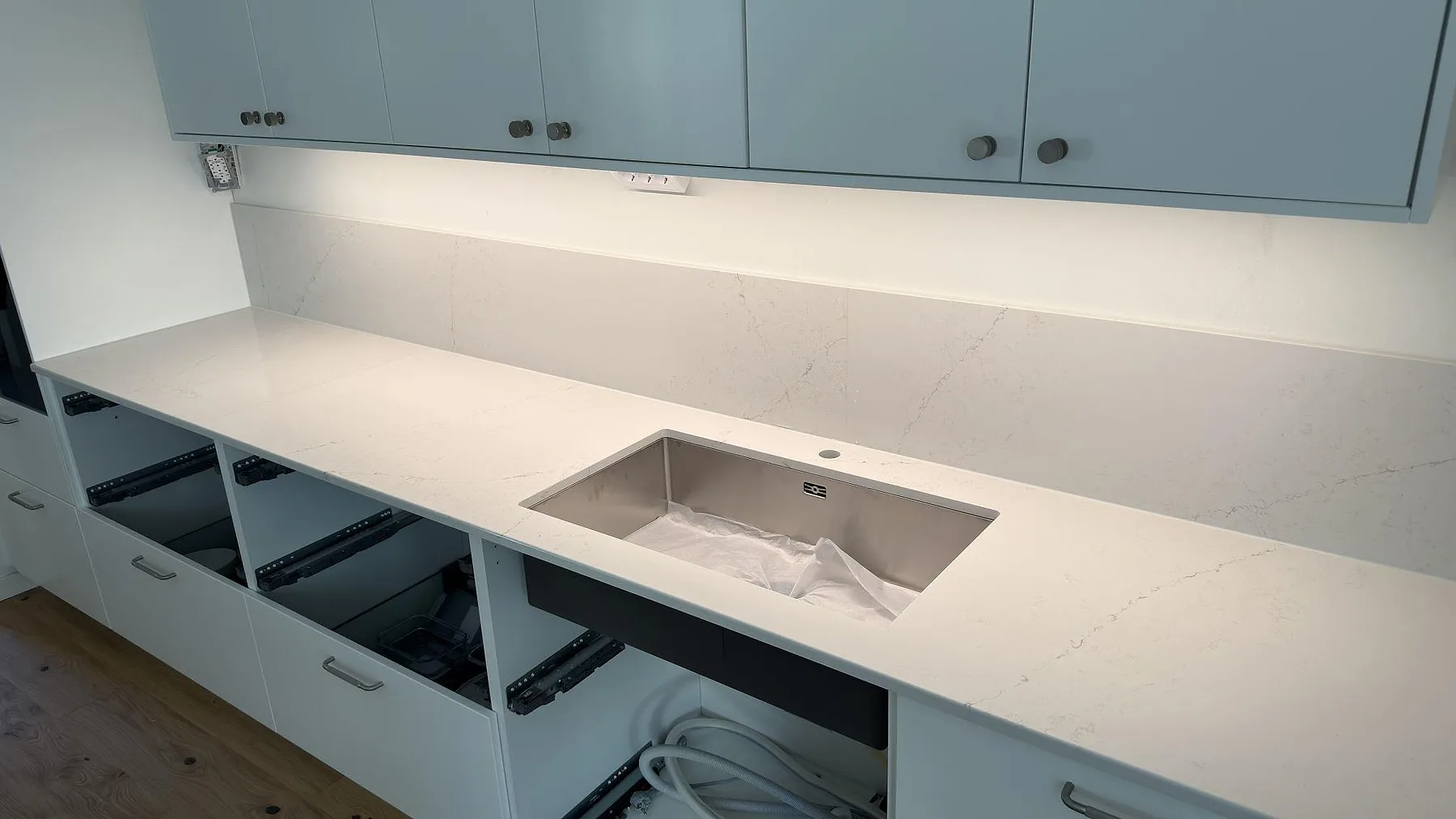 Väggmonterad köksbänkskiva i polerad Silestone Siberian frost med diskho och lågt stänkskydd i ett kök i Norrköping.