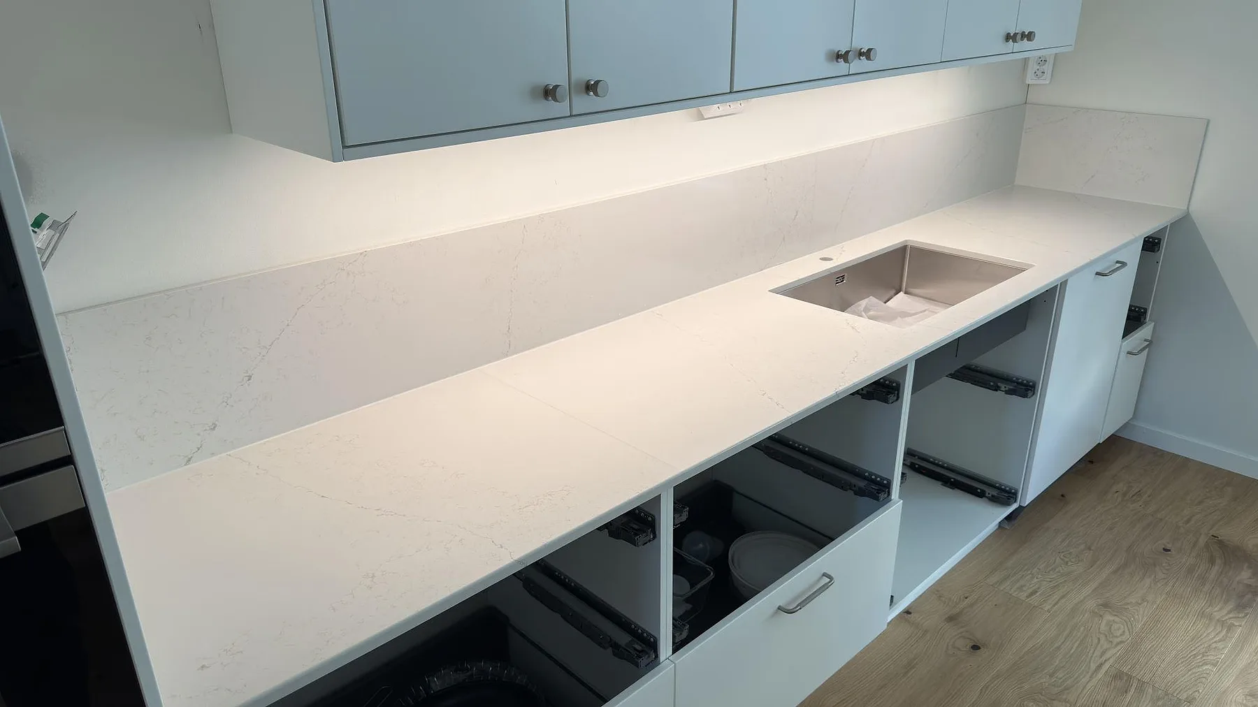 Lång köksbänk i polerad Silestone Siberian frost med samma stänkskydd och diskho vid väggsidan i Norrköping.