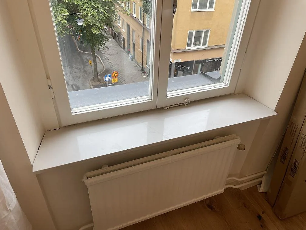 Fönsterbänk i polerad Silestone Siberian Frost, vit kvartskomposit, monterad ovanför radiator i Stockholm.