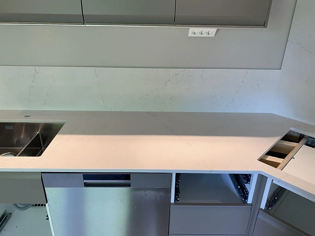 Lång arbetsyta i polerad Silestone Siberian frost med diskho, hällöppning och stänkskydd i köket i Veberöd.