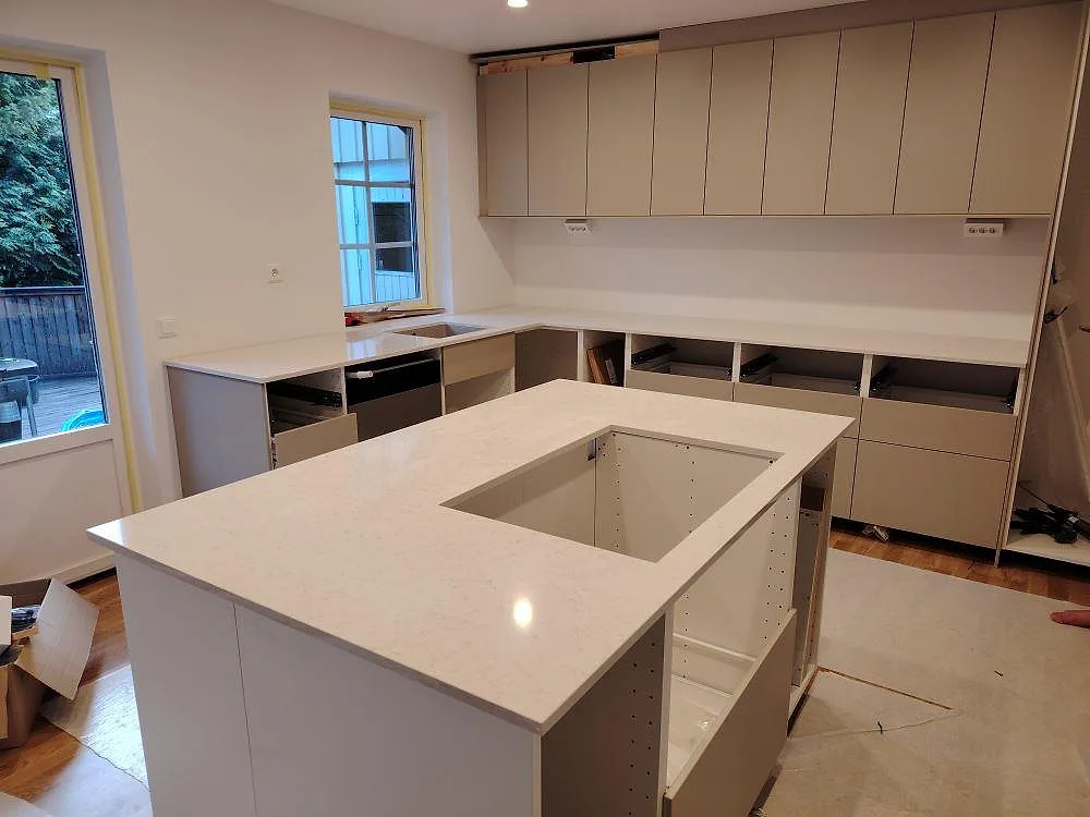 Polerad kompositbänkskiva i Silestone Snowy Ibiza med köksö och lång väggbänk under montering i Åkersberga.