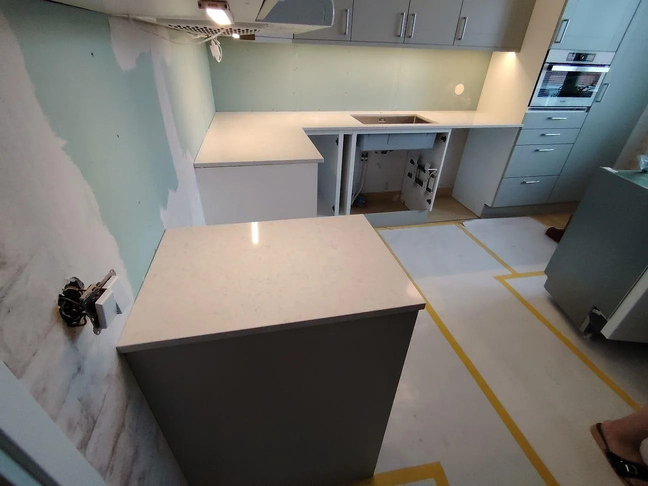 Köksbänkskiva i vit Silestone Snowy Ibiza, polerad kvartskomposit, på köksö och bakre bänkrad mot turkosgrön vägg i Åkersberga.