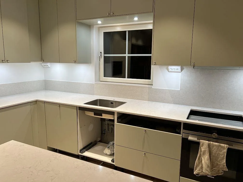 Närbild av polerad Silestone Snowy Ibiza som köksbänk runt fönster, med synlig diskhozon och spiszon i Åkersberga.