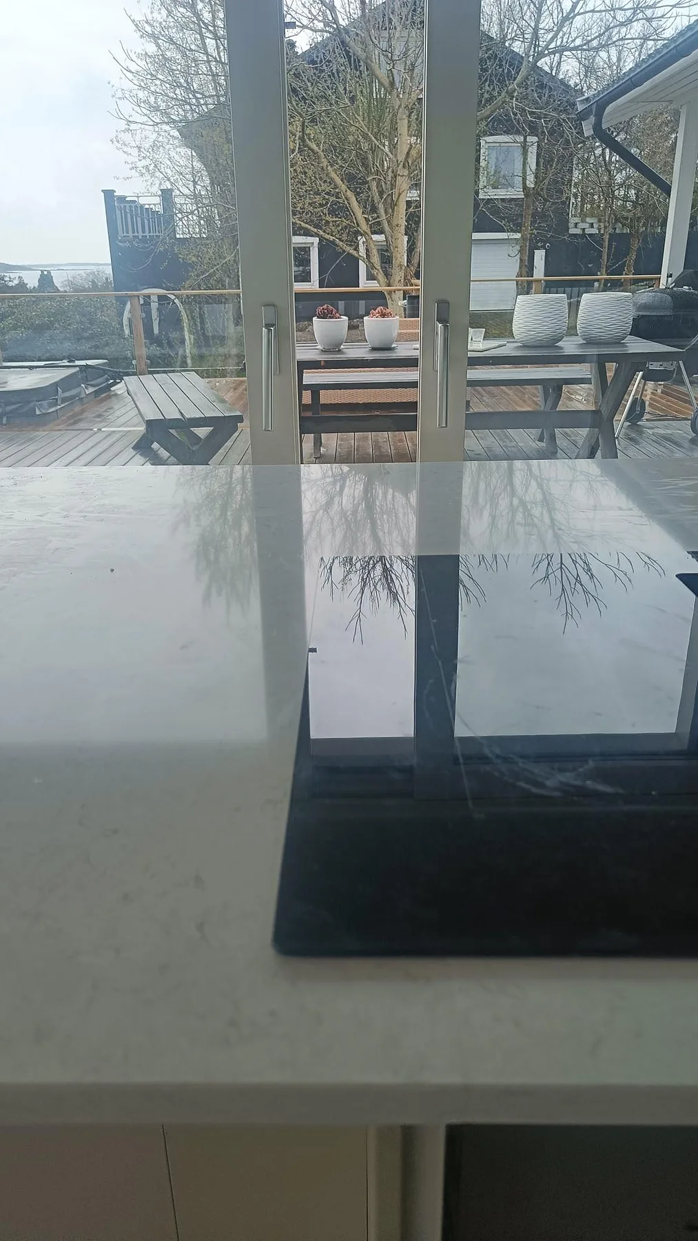 Blank polerad Silestone Snowy Ibiza på köksö med reflektioner från stora fönster och havsutsikt i Åskloster.