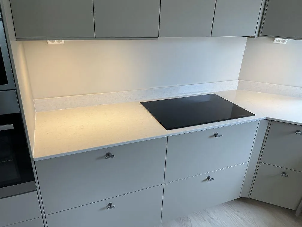 Polerad köksbänkskiva i vit Silestone Snowy Ibiza med svart häll och 12 mm stänkkant i kök i Älta.