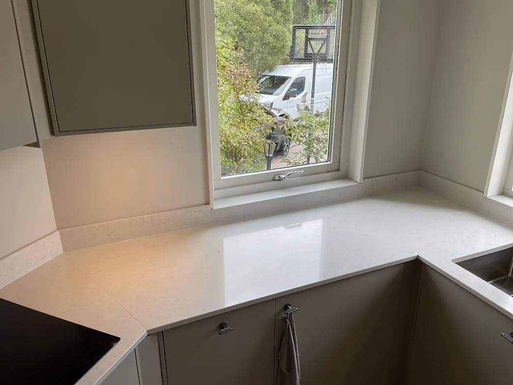 Närbild av polerad Silestone Snowy Ibiza-bänkskiva vid fönsterhörn med ljus ådring och låg stänkkant i Älta.